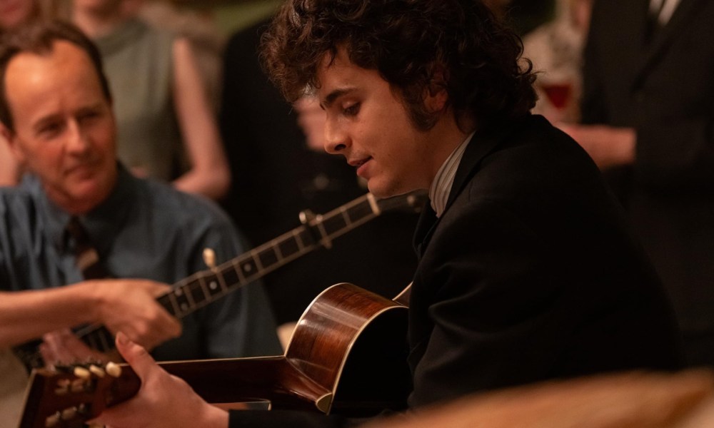 Timothee Chalamet holds a guitar and plays in A Complete Unknown.