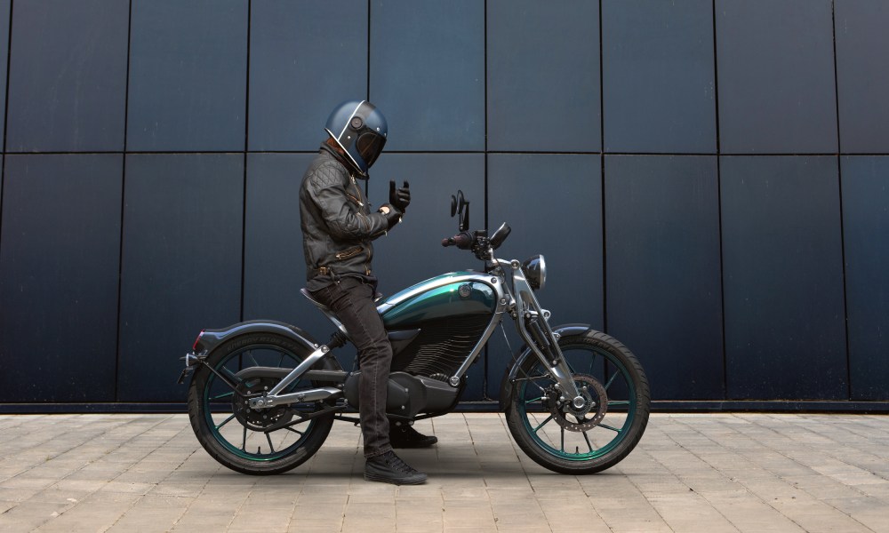 Rider astride a Royal Enfield brand Flying Flea FFC6 adjusting his gloves right side view.