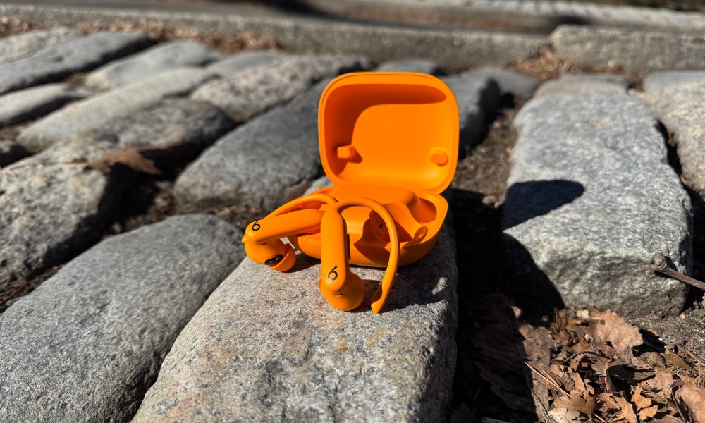 The Beats Powerbeats Pro 2 in orange sitting in front of their case on a stone.